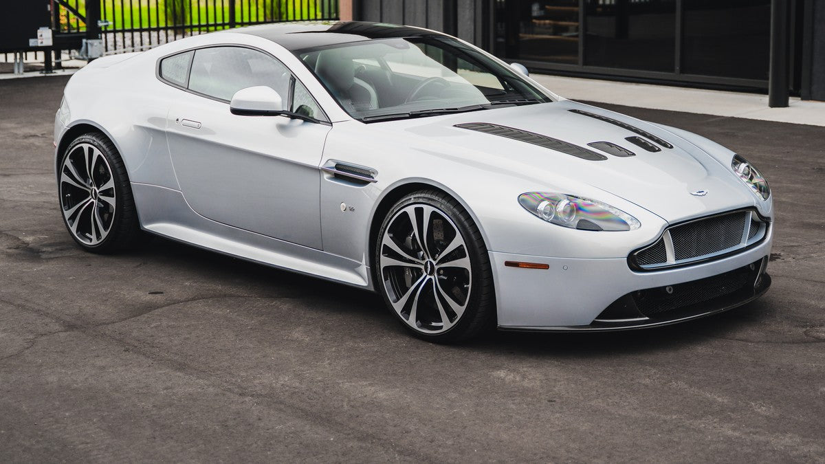 Silver Aston Martin coupe photographed outdoors.