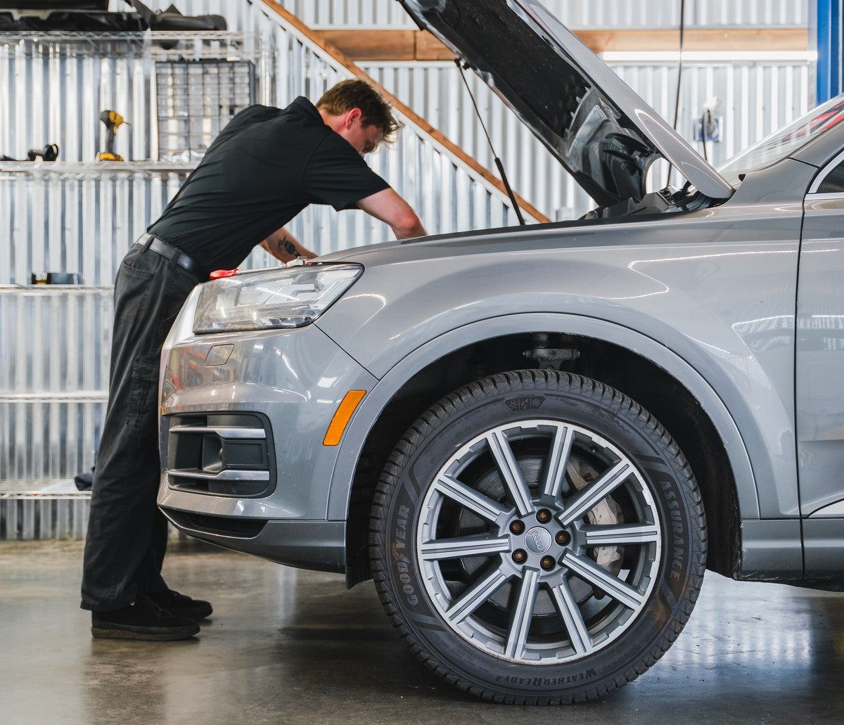Technician leaning into the open engine bay of a silver Audi SUV.