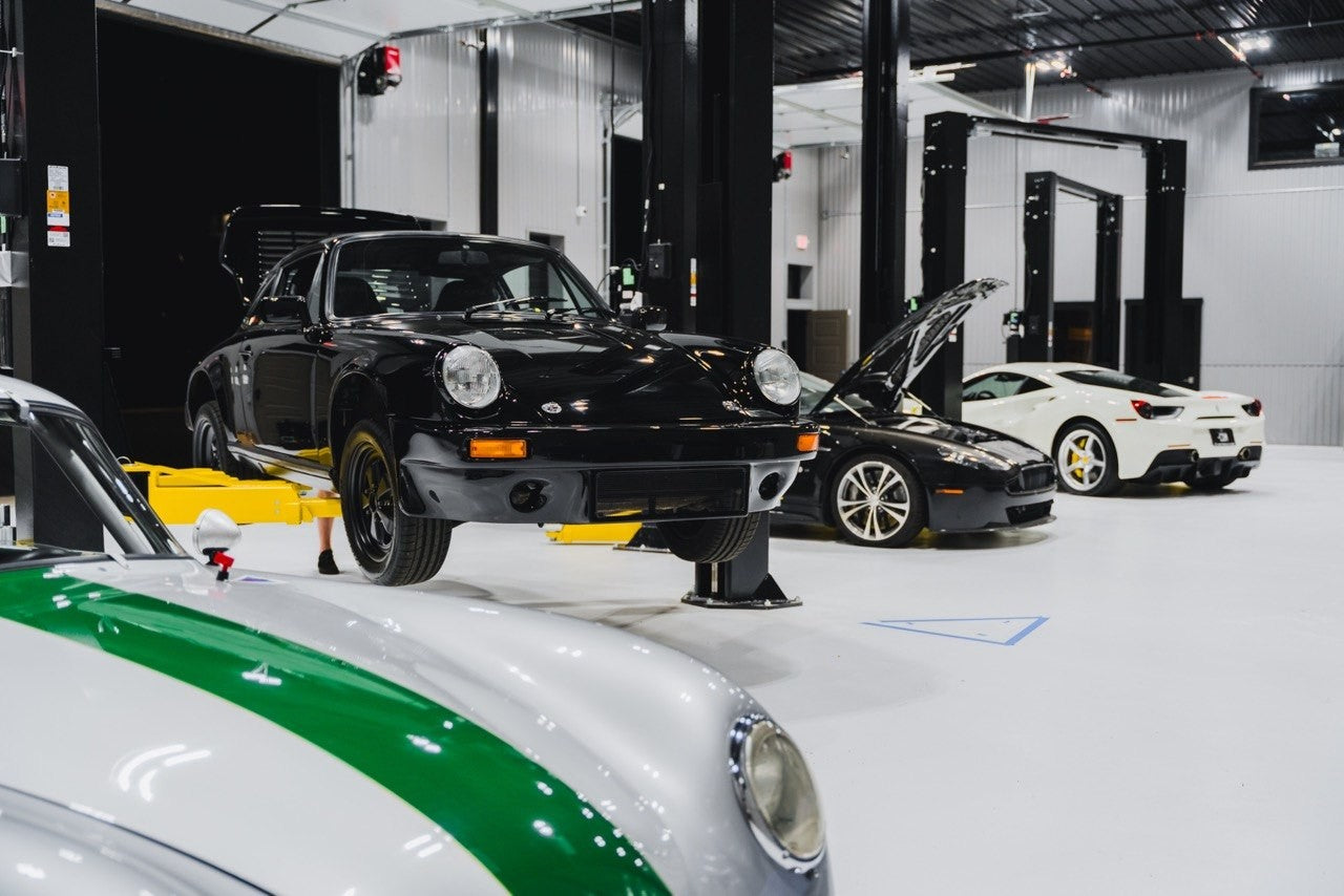 Classic Porsche on a workshop lift with other vehicles in neighboring bays.