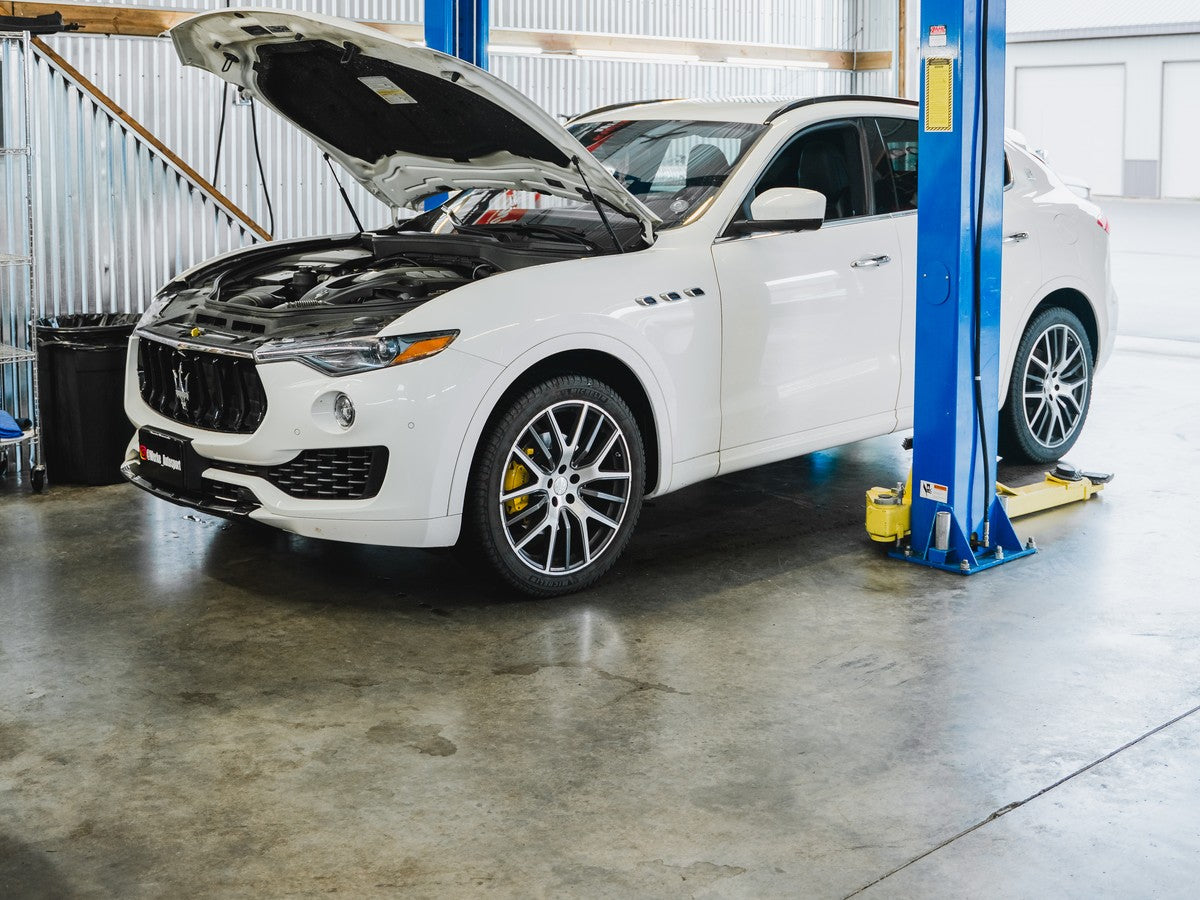 White Maserati SUV with its hood open between workshop lift posts.